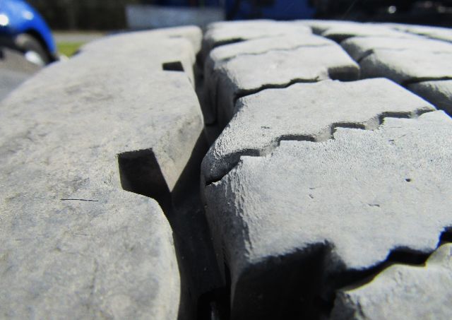 Close-up of treaded truck tire with deep cracks and wear visible between the treads.