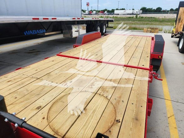 Flatbed trailer with wooden deck and red frame, showing a large circular cutout on the wood. Side rails and ramp are visible.