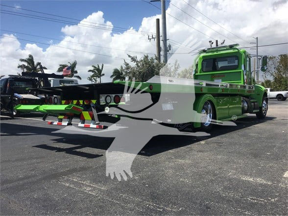 Green Peterbilt 337 tow truck on trailer with loading equipment in lot. Visible text: None legible on truck from distance.