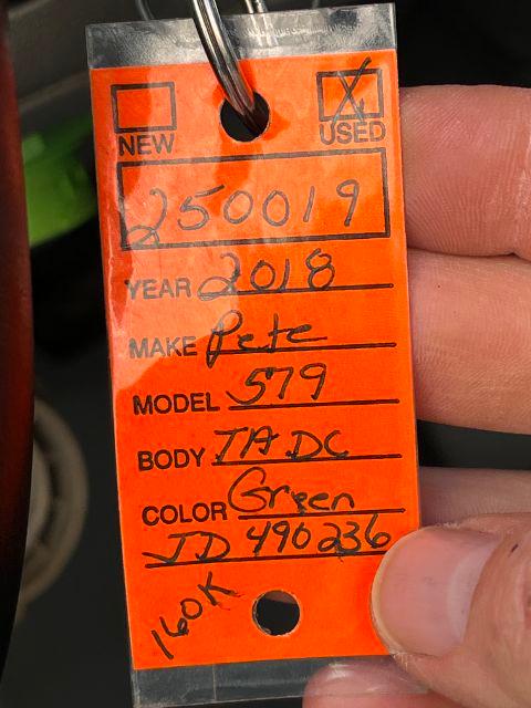 Orange inventory tag attached to a Peterbilt 579 showing handwritten details: Year 2018, Make Pete, Model 579, Body IA DC, Color Green, JD 496236, 160K