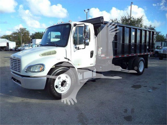 Freightliner Business Class M2 106 dump truck in a lot with white cab and black dump bed, foreground view.