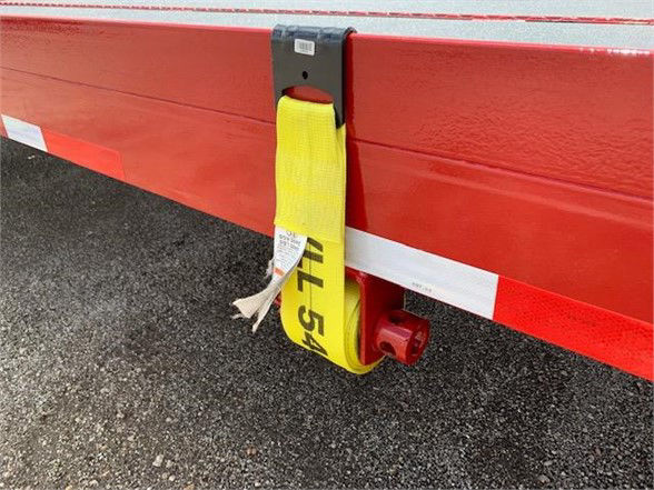Flatbed trailer edge with yellow strap and red underside showing latch and reflective markings.