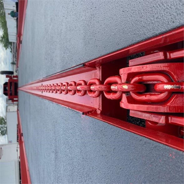 Red chain tie-down track on a drop deck container trailer, showing a close-up of the chain link and rail.