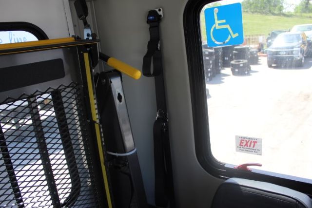 Ford E450 shuttle bus interior showing wheelchair securement strap and safety rail near window with a handicap placard.