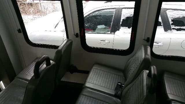 Bus interior with row of grey seats, windows showing outside snow and a white vehicle.