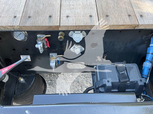 Trailer chassis with control valves, air line fittings, and toolbox visible in a small engine bay area; gauges and hoses present.