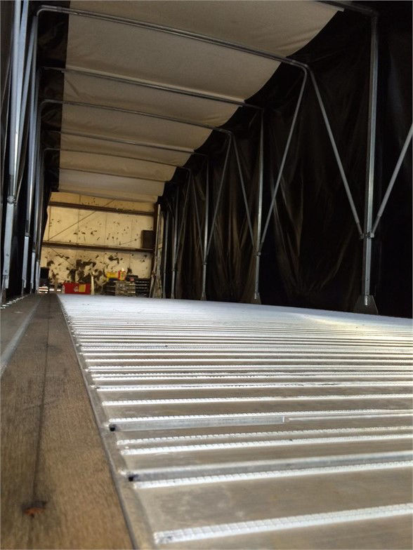 Inside a Fontaine tarp system trailer with metal ribbing and corrugated floor, showing interior framework and black tarp walls.