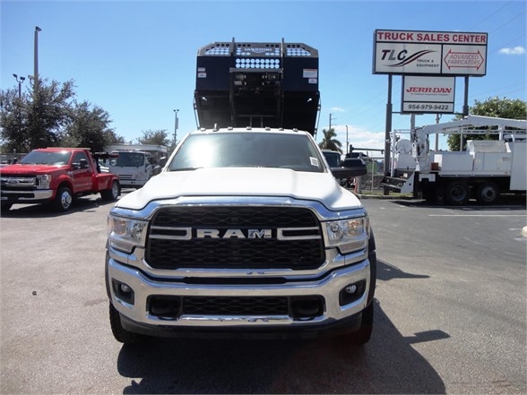 Front view of a white 2023 Ram 5500 HD hooklift truck with a heavy-duty hydraulic bed raised above cab.