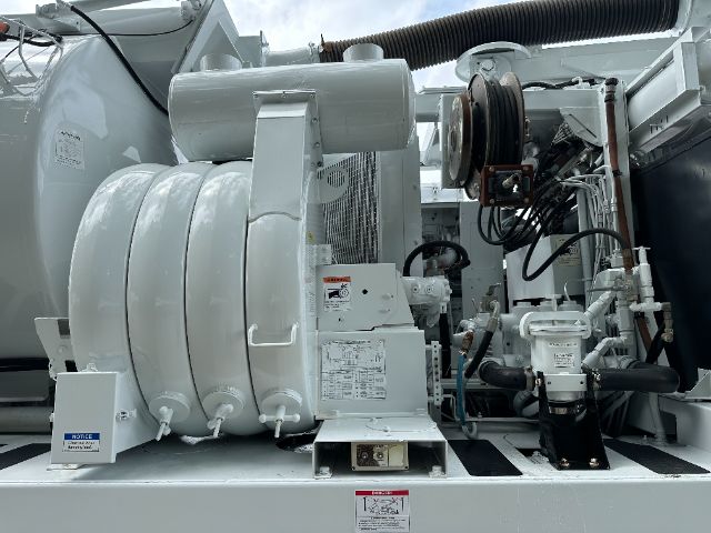 Peterbilt 340 vacuum truck engine bay showing high-pressure pump, hose reel, and control panel components with gray exterior and black hoses.