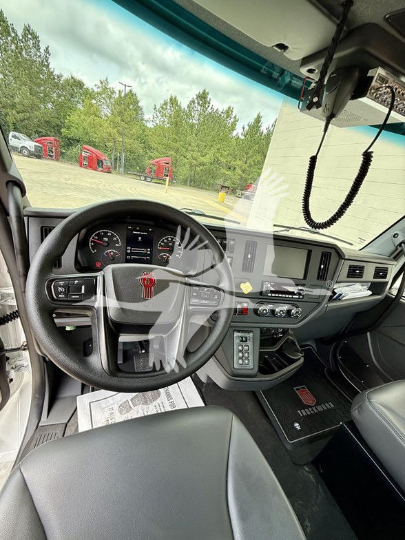 Kenworth T480 cabin interior showing steering wheel with red Kenworth emblem, dashboard gauges, center console with controls, and floor mats.