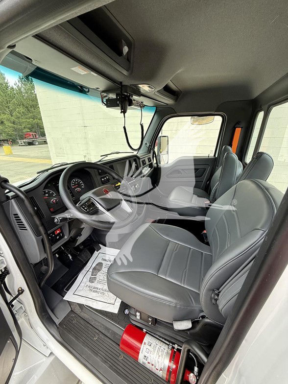 Kenworth T480 cab interior showing steering wheel, dashboard gauges, gray cloth seats, sun visor, overhead structure, and a red fire extinguisher mounted near the driver seat.