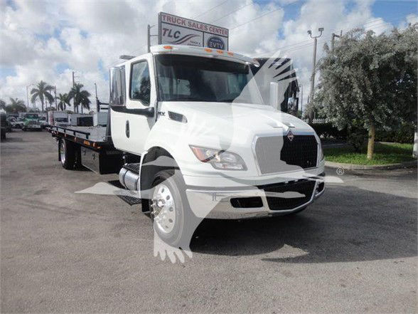 Tow truck with white cab and flatbed, International logo on grille. Sign on top reads 'TRUCK SALES CENTRAL TLC'. Side mirrors, headlights, and wheel wells visible.