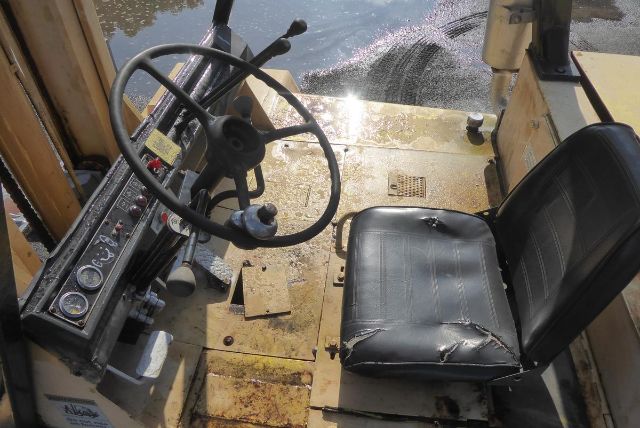 Caterpillar V225 operator seat and steering wheel in cab with control panel showing gauges and levers.