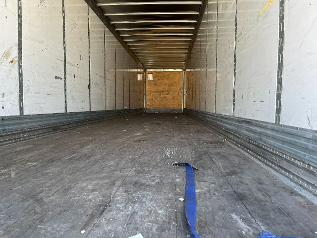 Interior of a long cargo trailer with wooden rear door, metal side walls, and a blue strap on the floor.