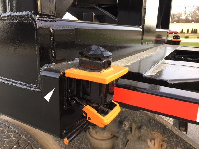 Trailer hitch or support bracket with orange protective bumpers on a black Wabash tipper trailer chassis, welding seams visible, tire and red reflective stripe in view.