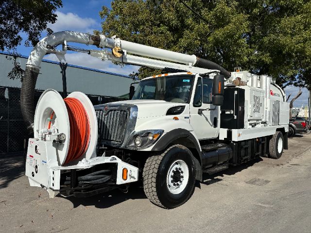 International vacuum truck with long hose reel and mounted vacuum apparatus, white cab and equipment, large front grille, black fender arches, side mirrors, and red hose on reel.