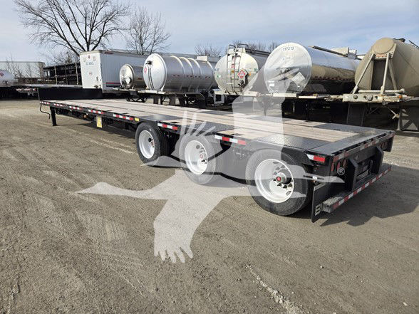 Tri-axle steel drop deck trailer with dual rear axles and multiple support beams, showing tanks in background.