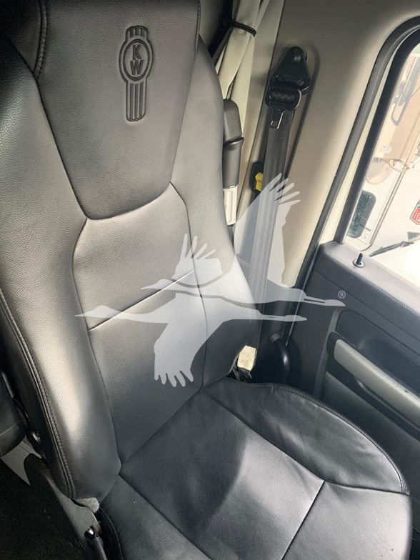 Kenworth T680 truck interior seat with leather upholstery showing an embossed Kenworth logo on the headrest. The image shows a black seat, door panel, and seatbelt, with a watermark overlay.