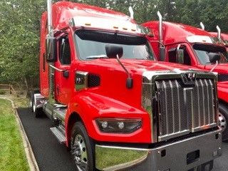 Truck front view showing 2023 Western Star 4900 Conventional Sleeper with large chrome grille and red paint.