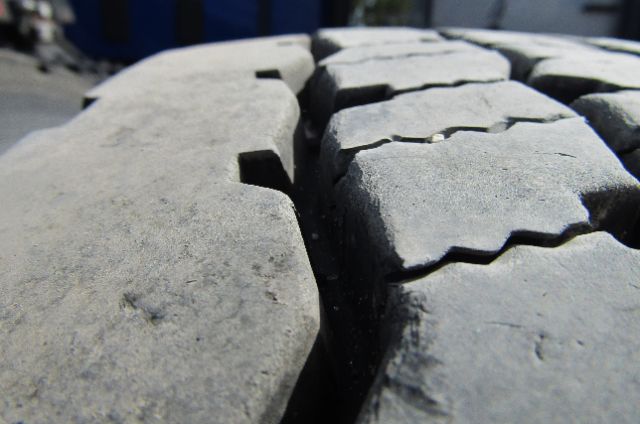 Close-up of large truck tire treads with deep grooves and wear.