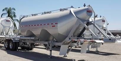 Pneumatic dry bulk trailer with a cylindrical aluminum tank mounted on a dual-axle chassis. The tank has a conical front and rear discharge hoppers, a top access hatch and piping along the top.