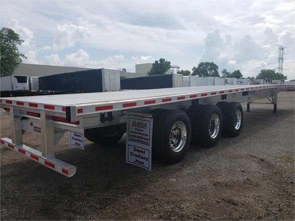 Flatbed trailer with multiple axles and aluminum deck showing reflective tape and wheels.