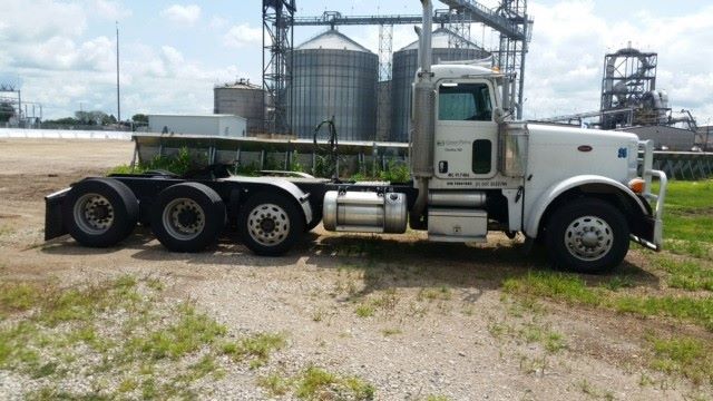 Peterbilt 379 conventional daycab truck side view showing white cab and multiple rear axles.