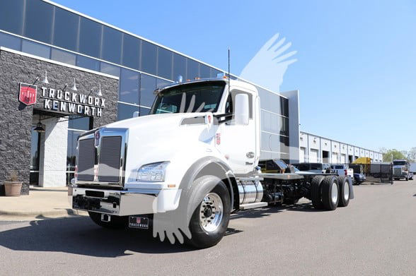 2026 Kenworth T880 cab and chassis truck in white exterior parked outside dealership with Kenworth sign in background.