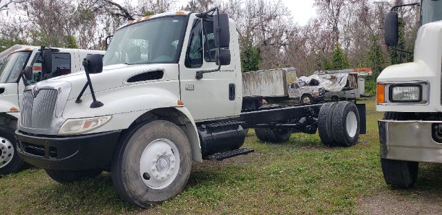 International cab and chassis truck in a yard, white cab with black chassis, side view, flatbed area for mounting body.