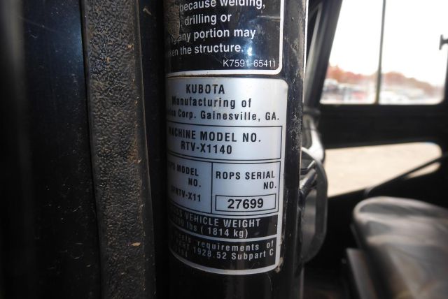 Kubota machine model label on a vertical surface showing 'KUBOTA Manufacturing of ... Corp. Gainesville, GA' and 'MACHINE MODEL NO. RTV-X1140'. Also shows 'ROPS SERIAL NO. 27699' and weight info.