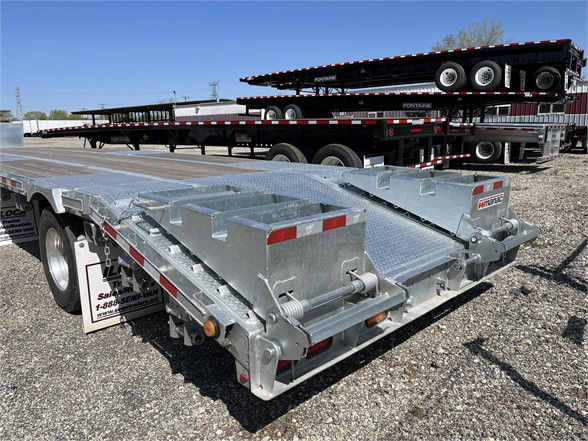 Manac steel stepdeck trailer in yard with other trailers in background; aluminum surface, dual-axle rear with ramps and storage boxes.