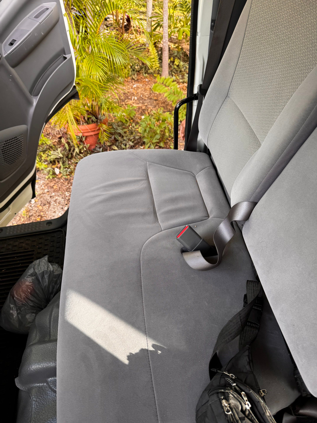 Isuzu NQR cab interior with front passenger seat and open door; gray fabric seats, seat belt, and a small bag visible near floor.