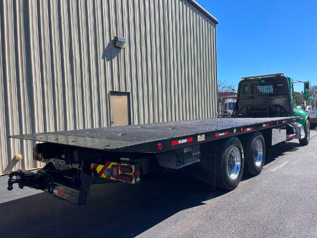 Peterbilt 348 rollback truck with a long flatbed trailer. Side view showing dual rear axles and green cab.