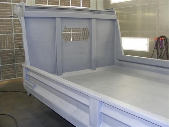 Truck bed side and headboard of a 14 ft dump body showing light gray primer, side rails, and a cutout with perforated panel.