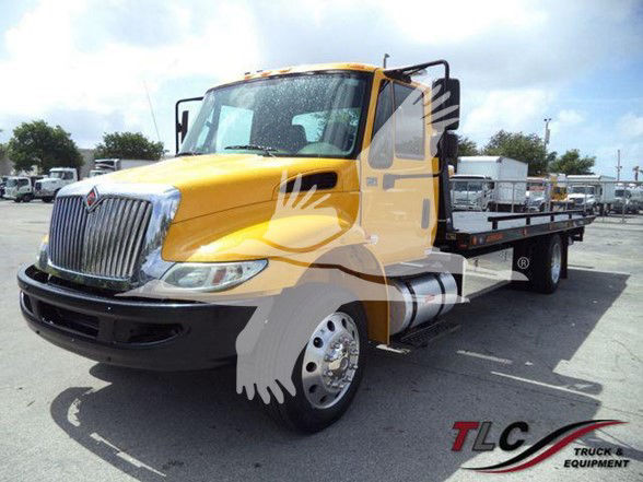 Truck bed tow truck 2019 International DURASTAR 4300 yellow cab with flatbed in a dealership lot.