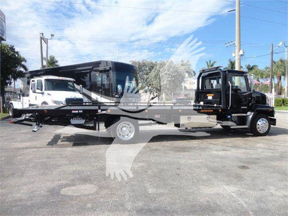 Tow truck winch truck in lot showing 2025 Mack MD6 with tow bed and transport trailer attached