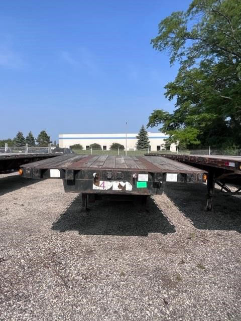 Flatbed trailer with wooden deck viewed from rear, 2006 Fontaine Elite listing. Stock number 54473 ELI, shows rear bumper, reflective tape, and gravel lot.