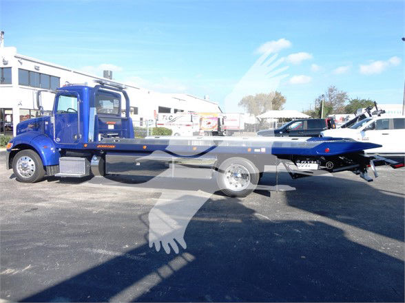 Blue Peterbilt 337 tow truck in a dealership lot with recovery equipment in the bed.