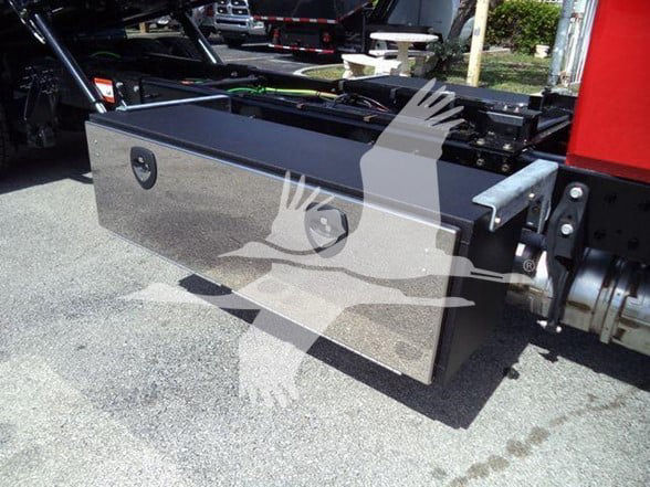 Truck tow setup with a large rectangular aluminum toolbox mounted on the side of the frame, two circular recessed latches, and hydraulic components in the background.