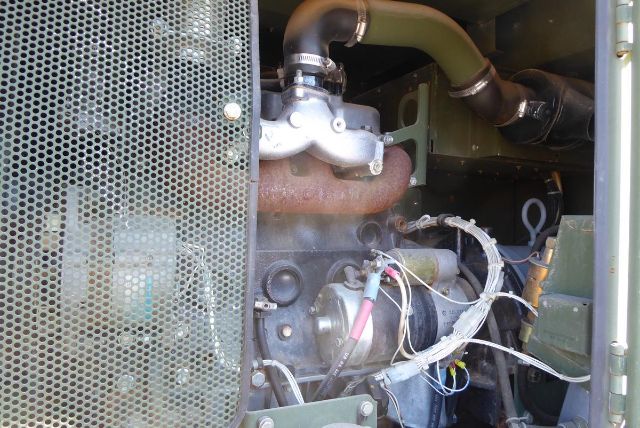 Truck engine bay showing exhaust manifold, turbocharger, various hoses, wiring, and a radiator grille on the left side.