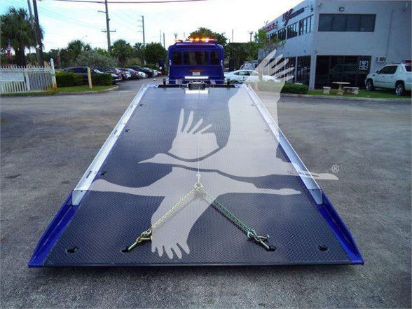 Tow truck flatbed with blue frame and a bird logo overlay, rear view showing the ramp deck and wheel chocks.