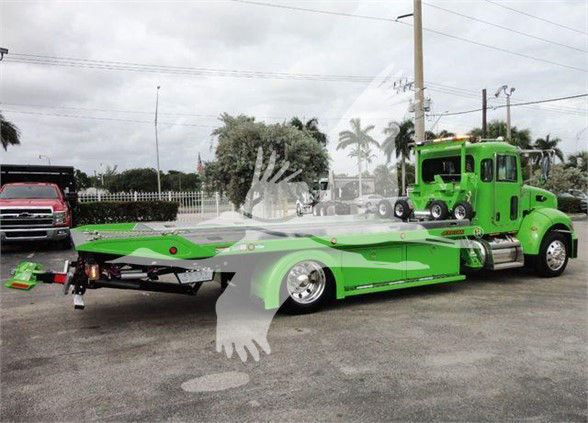 Green Peterbilt 337 tow truck with flatbed, side view showing long low bed and cab.