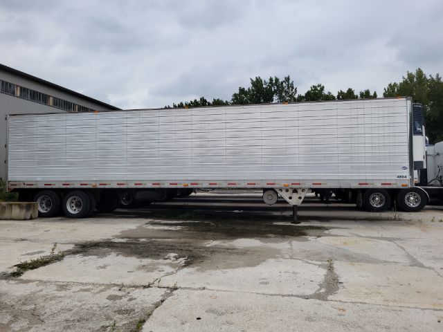 Trailer with a long silver reefer body and tandem axles parked, showing side of trailer. No legible text clearly visible from distance.