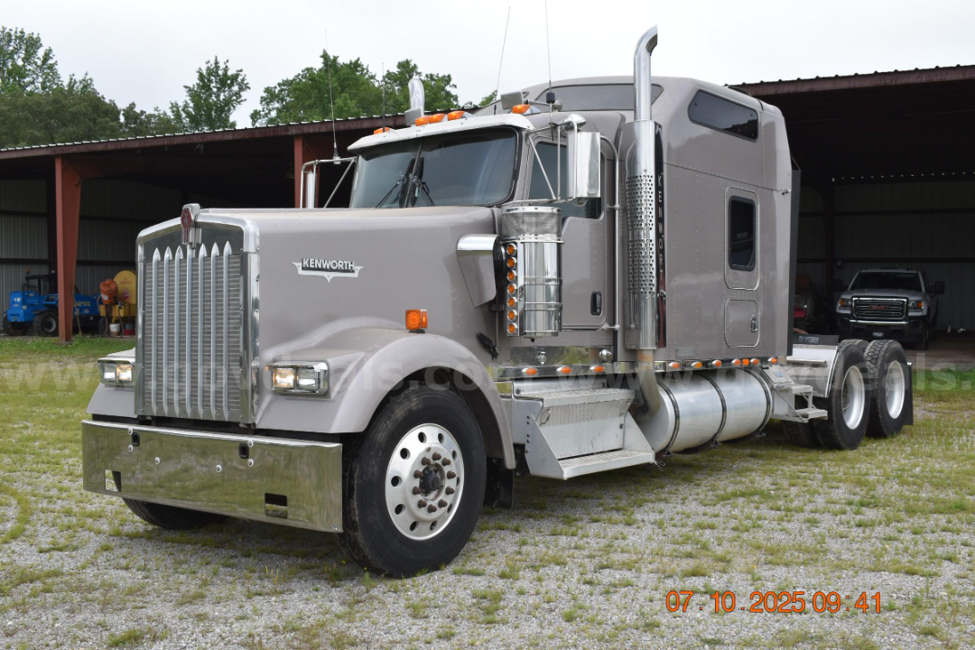 Kenworth W900 truck cab and chassis in silver with large chrome grille, stacked exhaust stacks, and dual rear axles; date stamp 07.10.2025 bottom right.