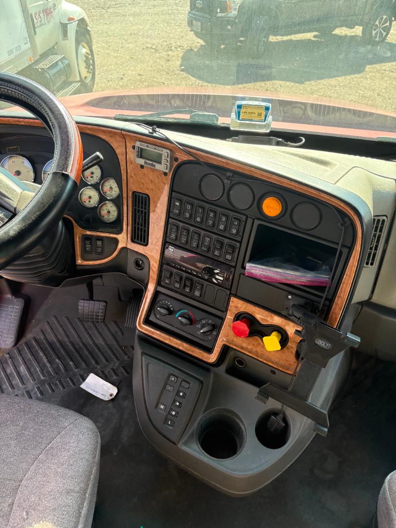 Interior of a 2016 International Prostar steering wheel and dashboard with wood trim, multiple gauges, switches, cup holders, and a mounted device on the dash.