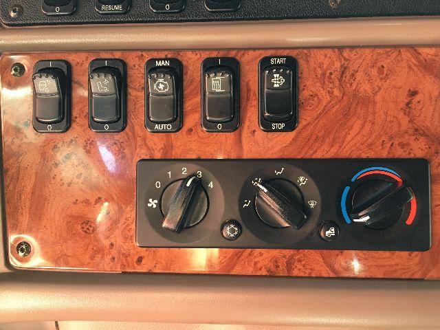 Peterbilt dashboard controls inwoodgrain panel showing climate knobs and ignition buttons.