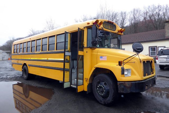 Bus appears to be a 2002 Freightliner yellow school bus with black trim, front bumper, and an American flag sticker on the front. Side door open, reflections in a puddle.