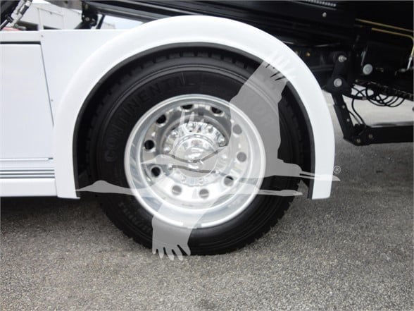 Front wheel and fender of a white 2023 Ram 5500 HD SLT with polished aluminum rim and black tire.