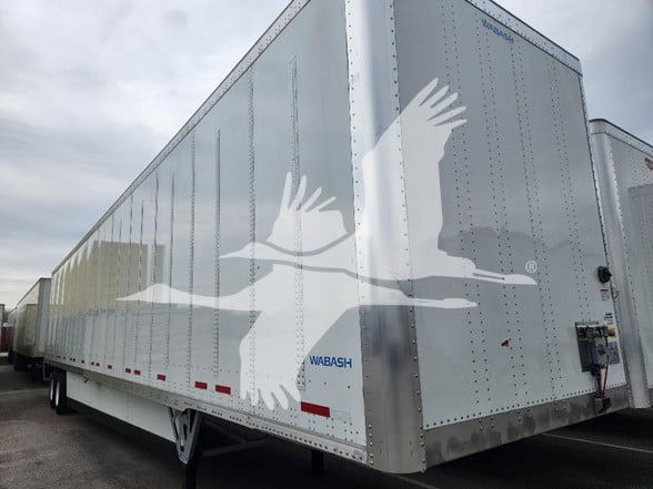 A silver Wabash trailer with a large white bird graphic on the side. The word WABASH appears near the lower front and there are red reflectors along the bottom edge.