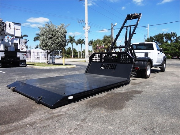 Ram 5500 HD hooklift truck with a large flatbed in a parking lot, white cab, black steel ramp and chainable lift mechanism.